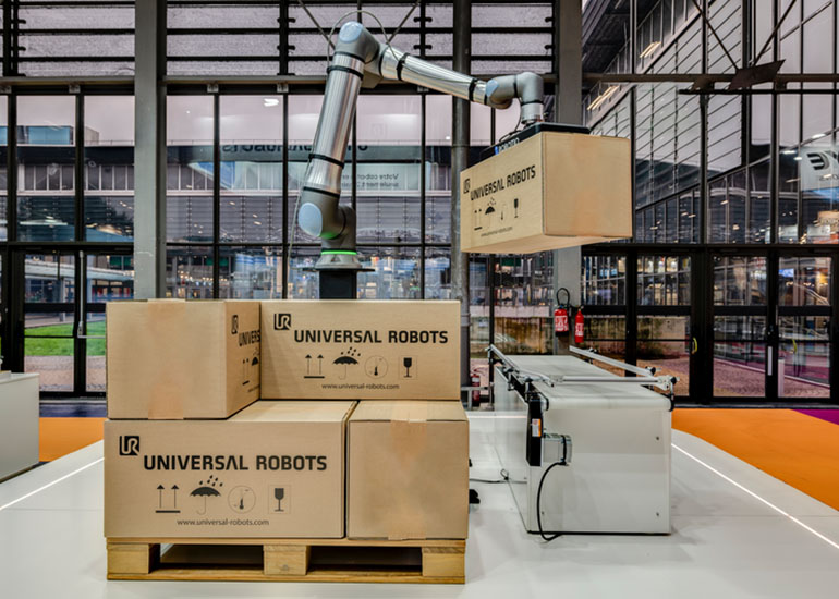 A UR20 collaborative robot lifting a box onto a partially built pallet. 