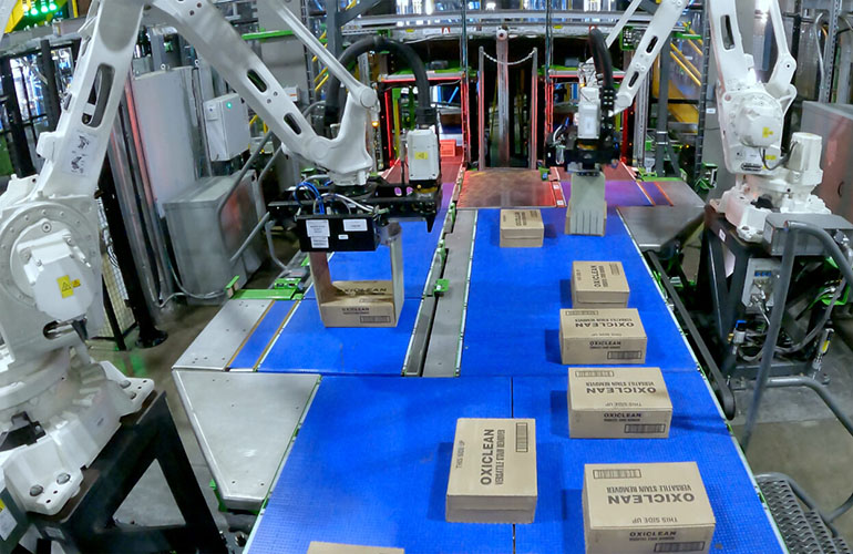 Two white robotic arms from Symbotic picking boxes on a blue table. 